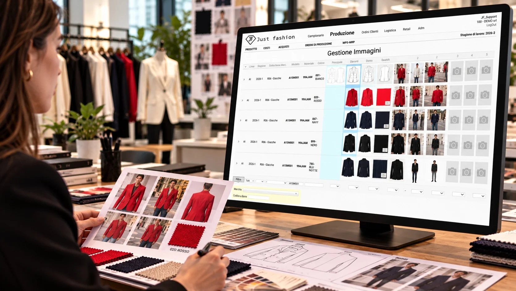 Ufficio prodotto con Just Fashion a monitor: Gestione Immagini della giacca A15M001 per i colori bianco, rosso, navy, nero e blu notte, con immagine principale, davanti, dietro, swatch e foto di vendita; sul tavolo le stampe delle foto e i campioni di tessuto